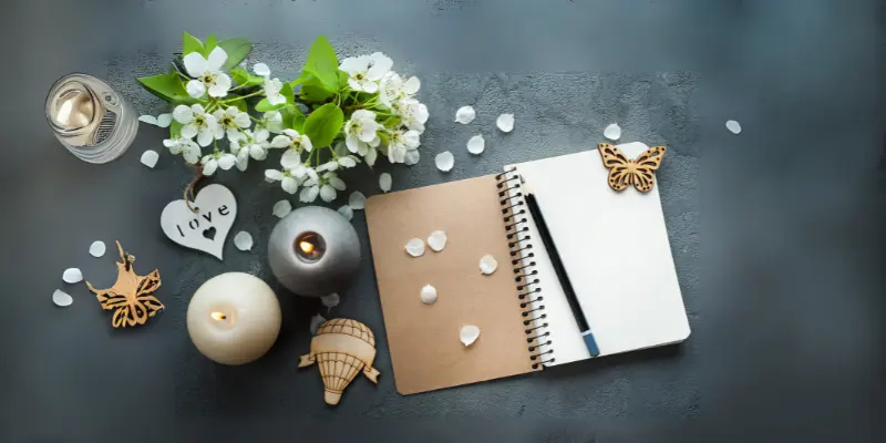 Daily Reflection Journaling Introvert Flat lay: Open journal with pencil, white flowers, and lit candles for daily reflection.