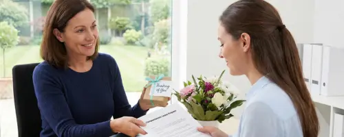 Employee Compassionate Leave Support Manager Gift A manager hands a compassionate leave request form and a "Thinking of You" gift to a grateful employee in a supportive office setting.