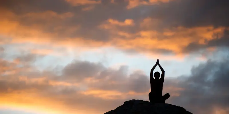 Mental Toughness Meditating Sunset Prayer Position Person meditating on a rock with hands in prayer position at sunset, symbolizing mental clarity, self-awareness, and inner strength