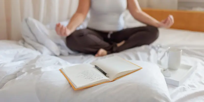 Mindfulness Journaling Morning Self Reflection Person practicing mindfulness and journaling in the morning, sitting on a bed with a journal, pen, and cup of tea, symbolizing mental clarity, consistency, and self-reflection.