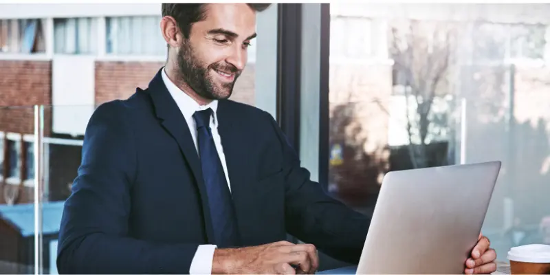 Smiling Man Working Laptop Financial Control Smiling man in a suit working on a laptop, symbolizing control, focus, and progress in managing financial tasks.