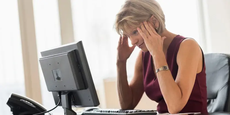 Woman Stressed Financial Woman sitting at a desk, holding her head in frustration and stress, symbolizing mental strain and decision paralysis due to financial worries.